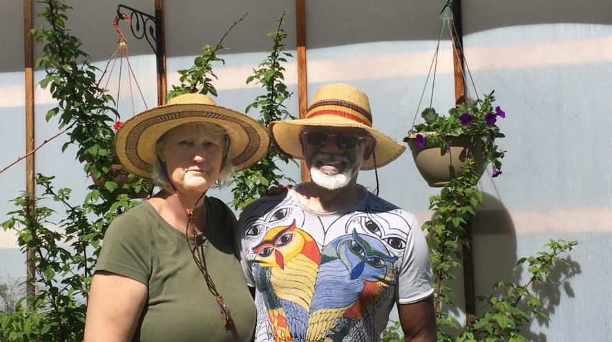 Birgit and Granville wearing straw hats on a sunny day in front of a colourful background.