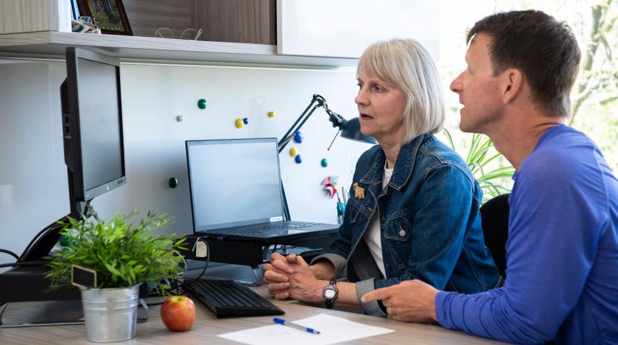 two people sitting in front of a computer, looking intently at the screen