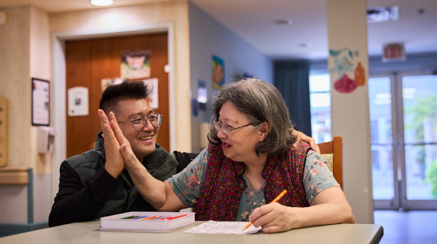 A son and mother holding hands in a long term care home