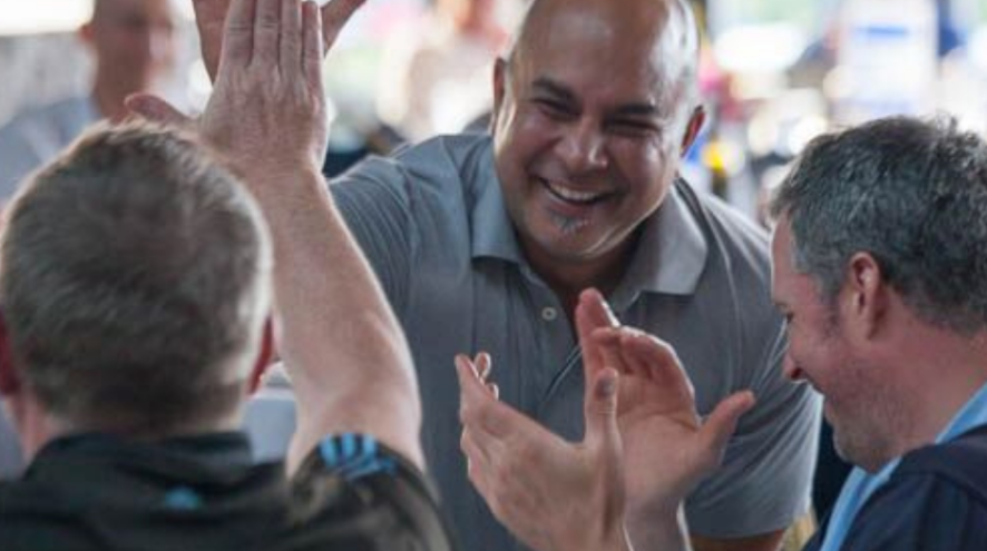 A group of men at a table, clapping and hi-fiving 