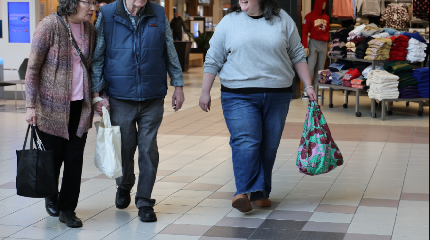 An elderly couple walking through the mall with a care partner 