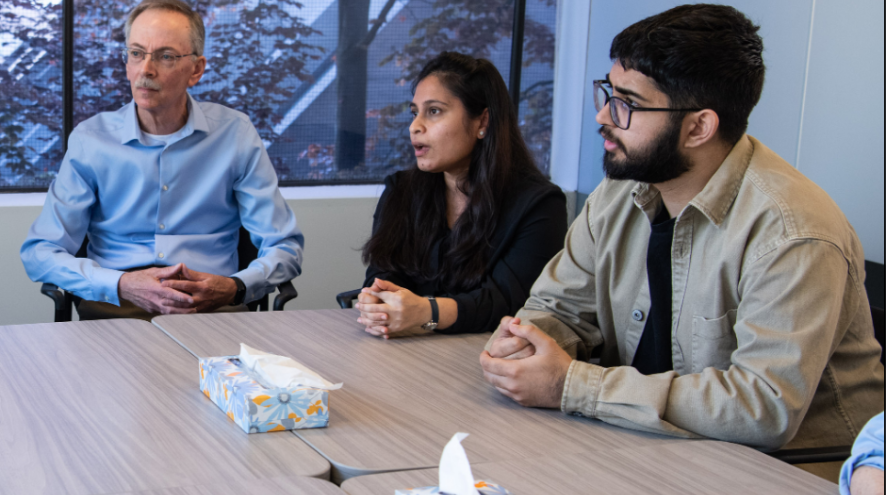Three adults sitting at a table listening to a presentation