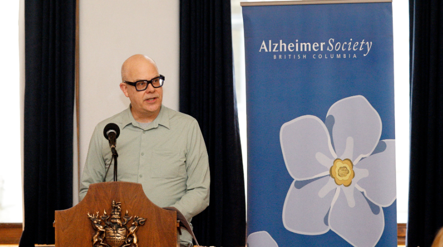 Person standing at a podium in front of a Alzheimer Society of B.C. banner