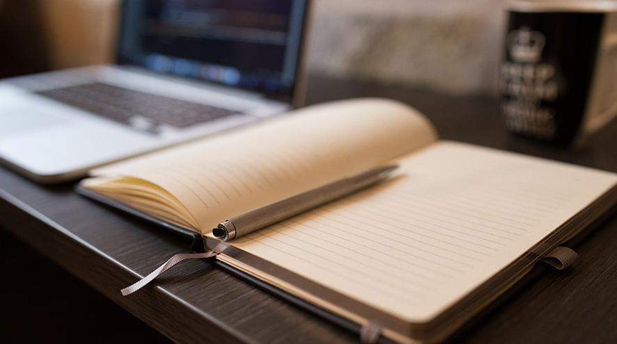 Picture of an open notebook sitting beside a laptop