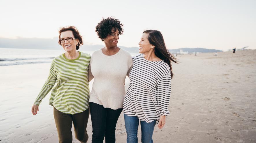 Three women walking arm in arm along a white sandy beach.
