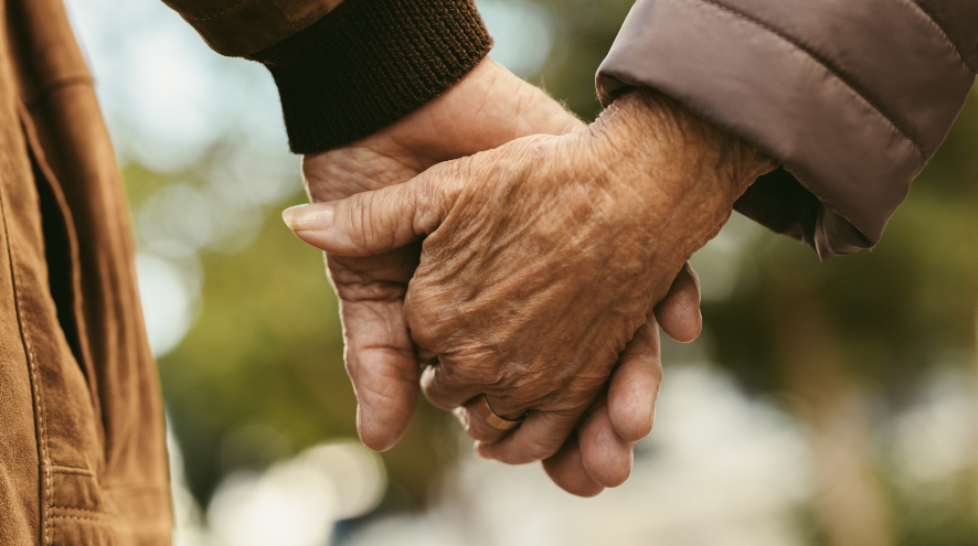 Close up photo of 2 seniors holding hands.