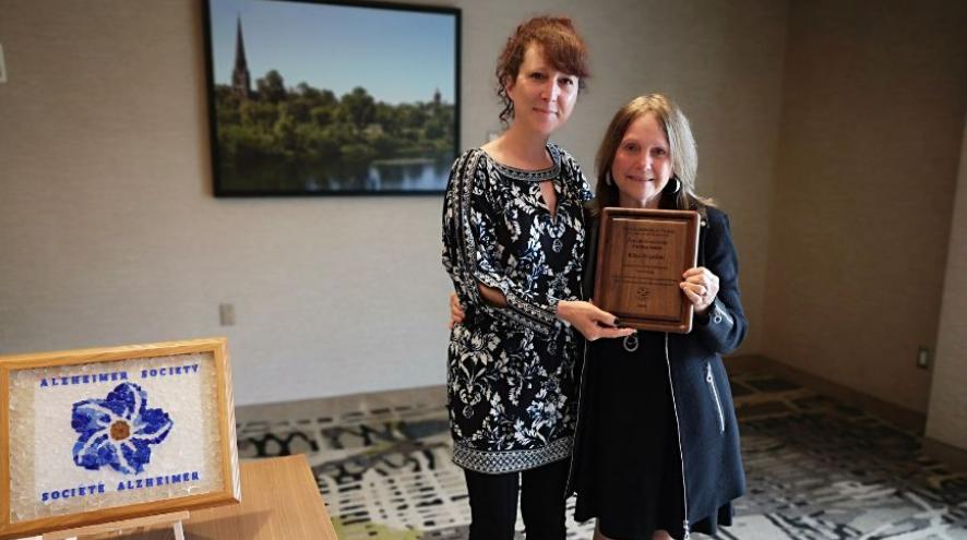 Photo of Riba being presented with the Pauline Spatz Leadership Award, a wooden plaque, by ASNB staff