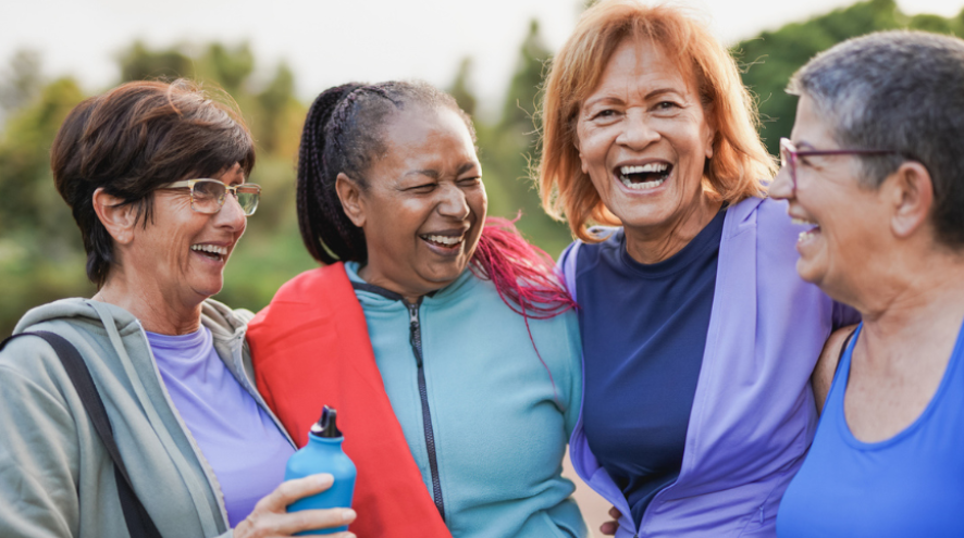 Four women in athletic gear with their arms wrapped around each other smiling