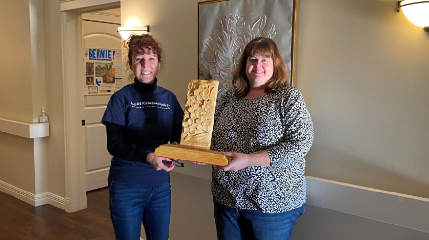 Photo of ASNB staff member presenting Grass Home Staff member with the forget-me-not trophy