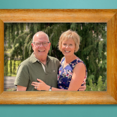 A photo of Peggy and her husband, Eric, in a wooden photo frame hanging on a teal wall