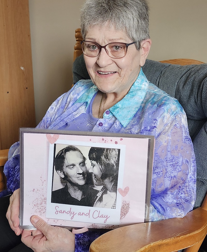 A woman holding a framed photo of herself and her husband