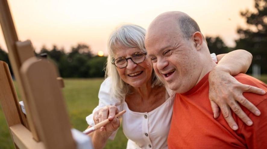 A woman holds a paintbrush with an arm around a man's shoulders