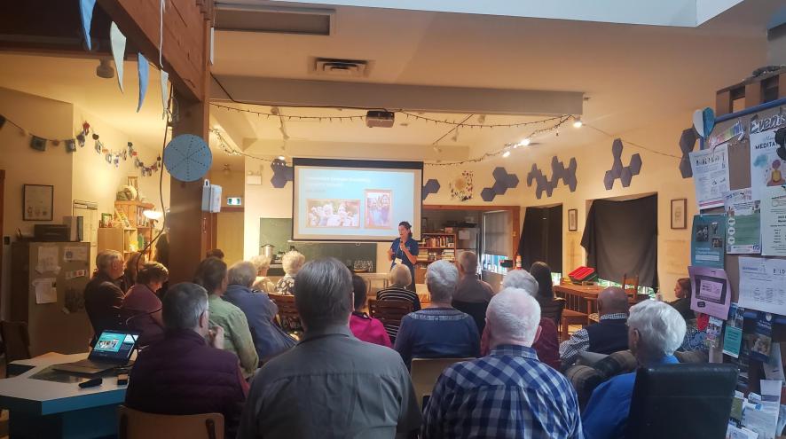 A group of people sit and watch a dementia presentation on a projected screen in a small room