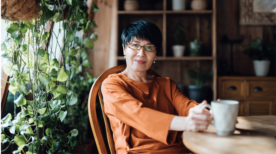 A midlife woman sitting at a table with a mug of tea