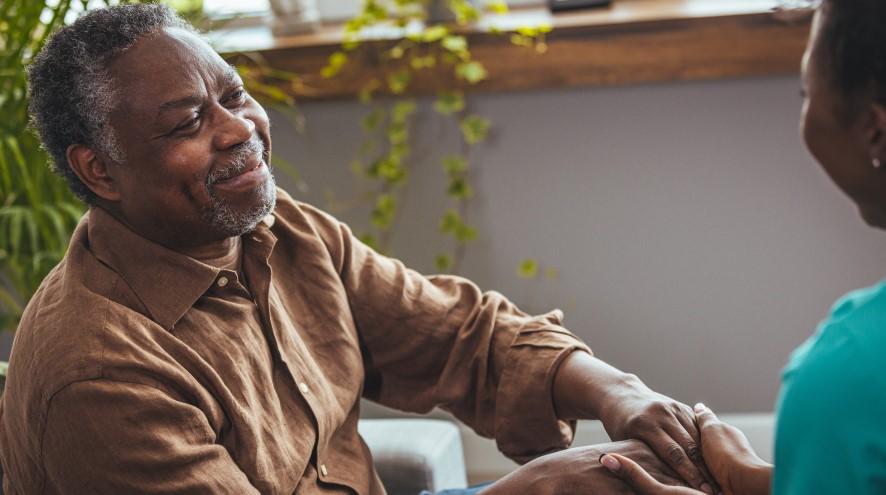 A smiling man in his 60s grasps the hands of a friendly relative.