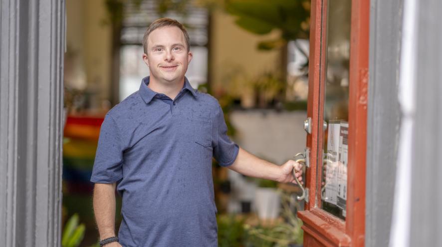 A man with Down syndrome stands at the entrance of his shop.