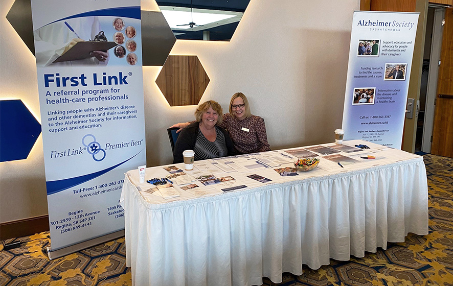 Alzheimer Society Staff sitting at a booth with resources and a banner about our First Link Program.