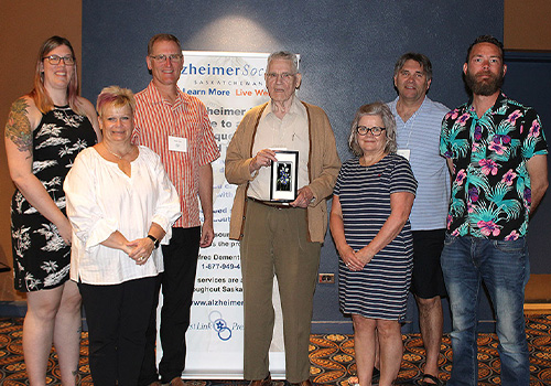 Ken Lee and his family are standing in front of an Alzheimer Society of Saskatchewan banner. Ken is holding his Corporate Leadership Award.