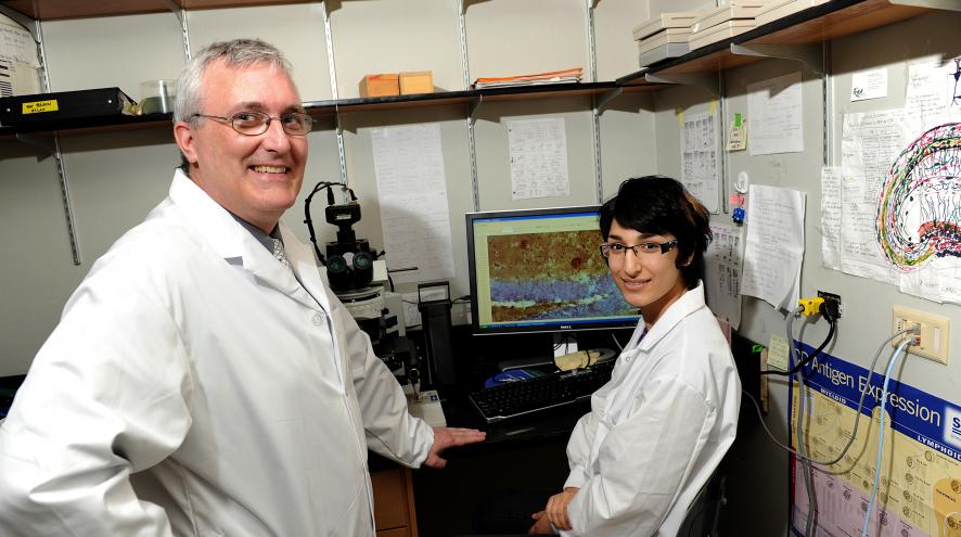 Dr. Darrel Mousseau standing beside a researcher who is seated at a desk.