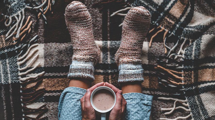 A picture of a person cozied up in a blanket with tea