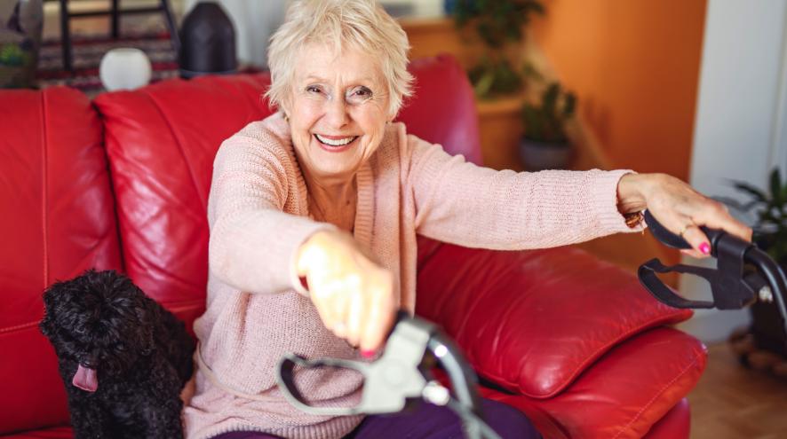 Image depicts older woman sitting on a couch while holding a walker