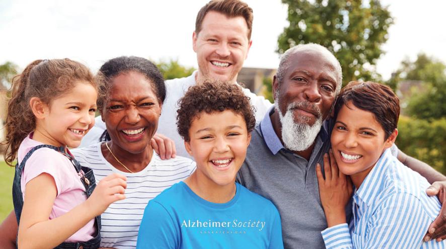A family standing together outdoors. Everyone is smiling and has their arms wrapped around each other. 