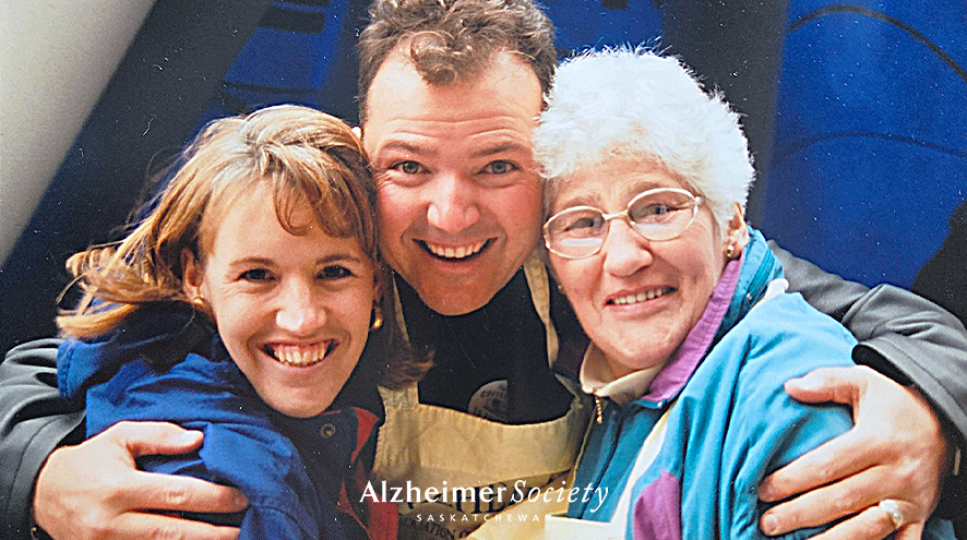 Three people are smiling and hugging. They are wearing Alzheimer Society aprons for fundraising.