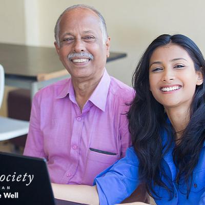 A father and daughter smiling as they complete an online questionnaire together.