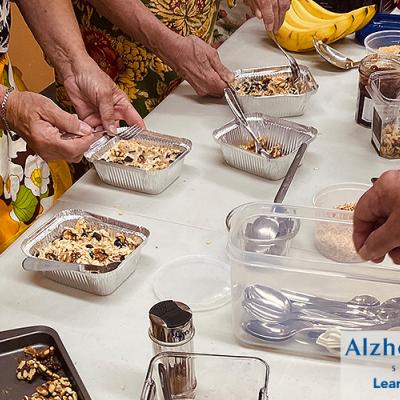 Multiple hands preparing individual pans of a dish with oatmeal and blueberries.