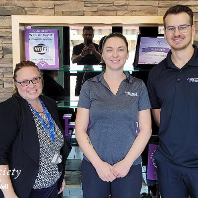 Our Dementia Community Coordinator standing next to two Anytime Fitness Yorkton representatives. Everyone is wearing black or dark grey colours and they are standing in front of a rock accent wall.