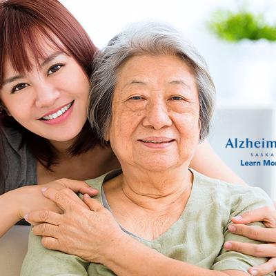 A younger woman has her hands lovingly wrapped around her aging mother, who is sitting down and smiling.