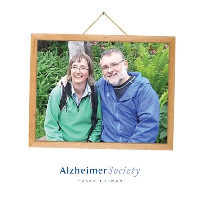 A picture frame with a photo of a woman and man sitting next to each other and smiling in a garden.
