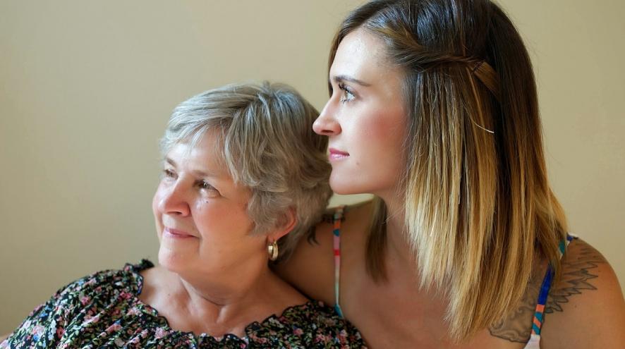 Head and shoulder shot of an adult woman hugging a senior woman. Both are looking to the left.