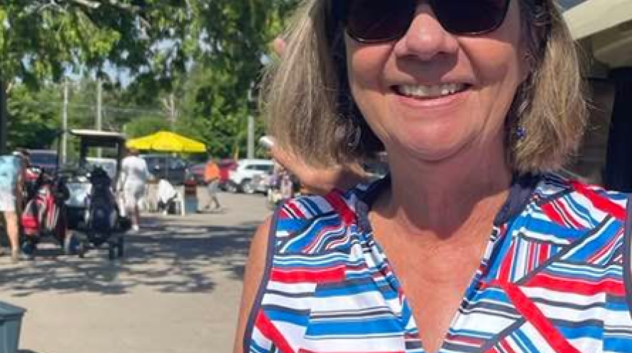 Head and shoulder picture of an older woman with shoulder length blond hair, wearing a golf visor and colourful shirt standing outside